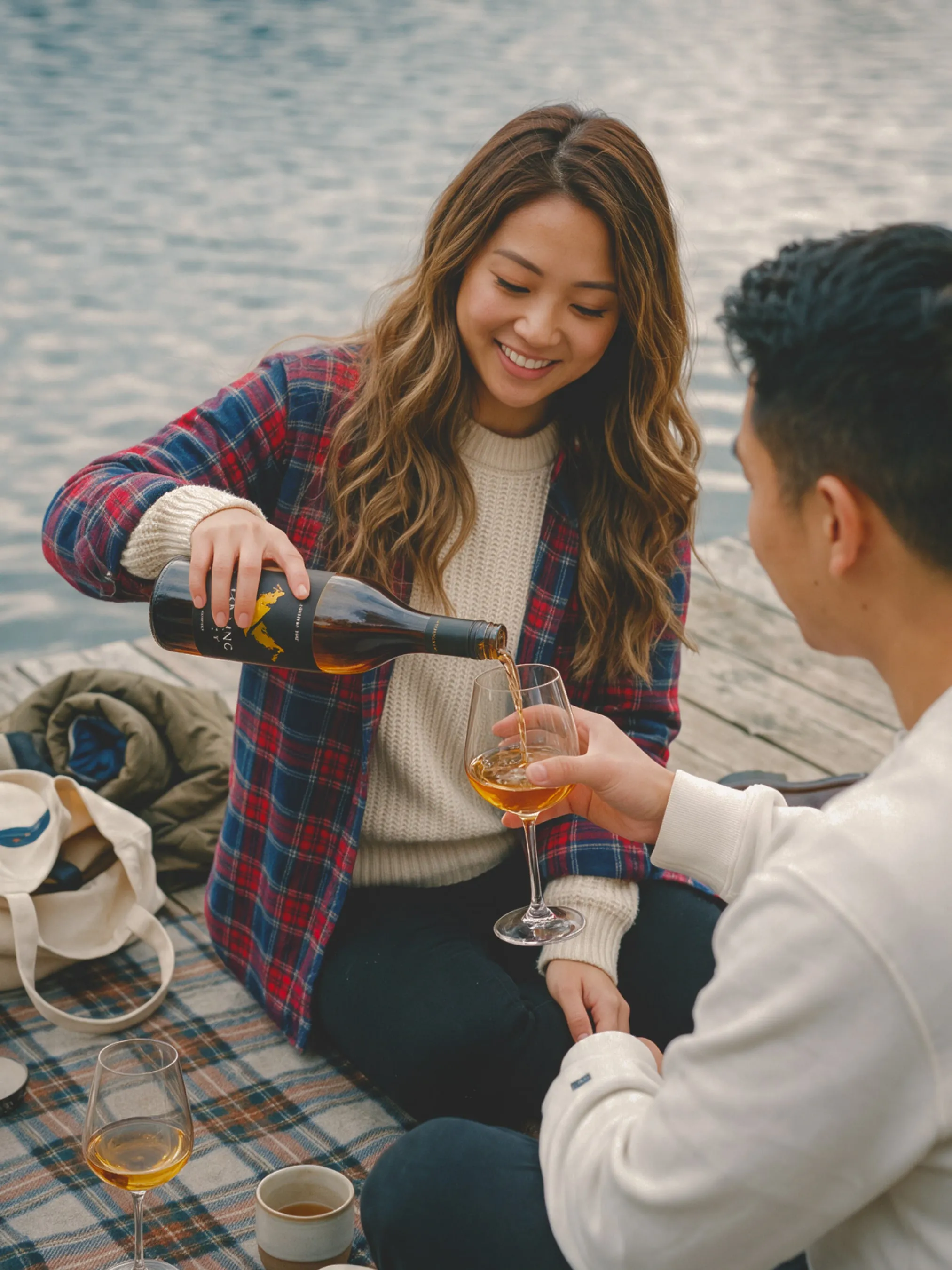 A couple pouring wine on a blanket by a lake